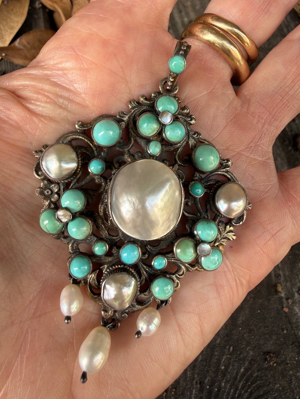 Austro-Hungarian silver pendant front view showing natural turquoise cabochons, mother of pearl center, and pearl drops, held in hand