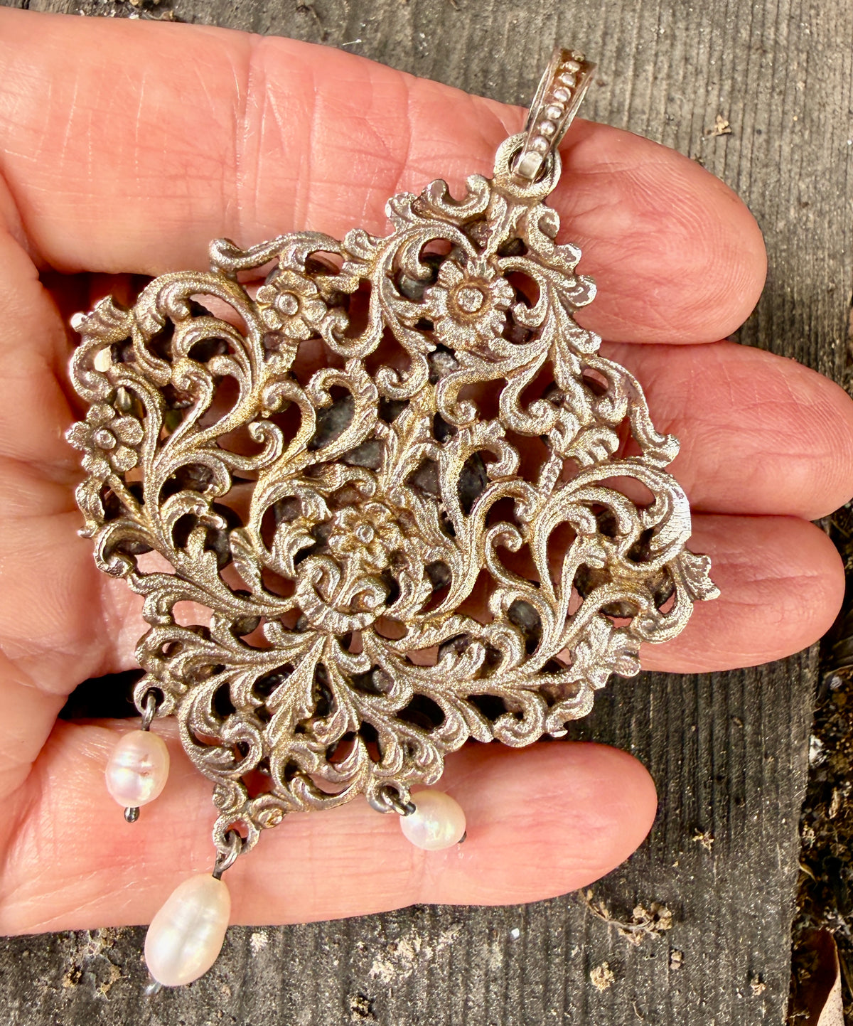 Austro-Hungarian silver pendant with open scrollwork, floral castings, and pearl drops, held in hand to show scale